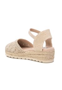 Sandalia de esparto beige con parte superior trenzada, punta abierta y correa en el tobillo. Presenta una suela intermedia de yute trenzado y una suela exterior de goma texturizada.