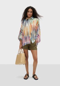 Colorful, lightweight blouse with stripes in orange, blue, and green. Worn with olive shorts and a gold handbag, featuring a textured pattern.