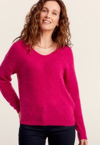 Pull en maille fuchsia avec un col en V, des manches longues et une finition douce et texturée. Associé à un jean foncé.