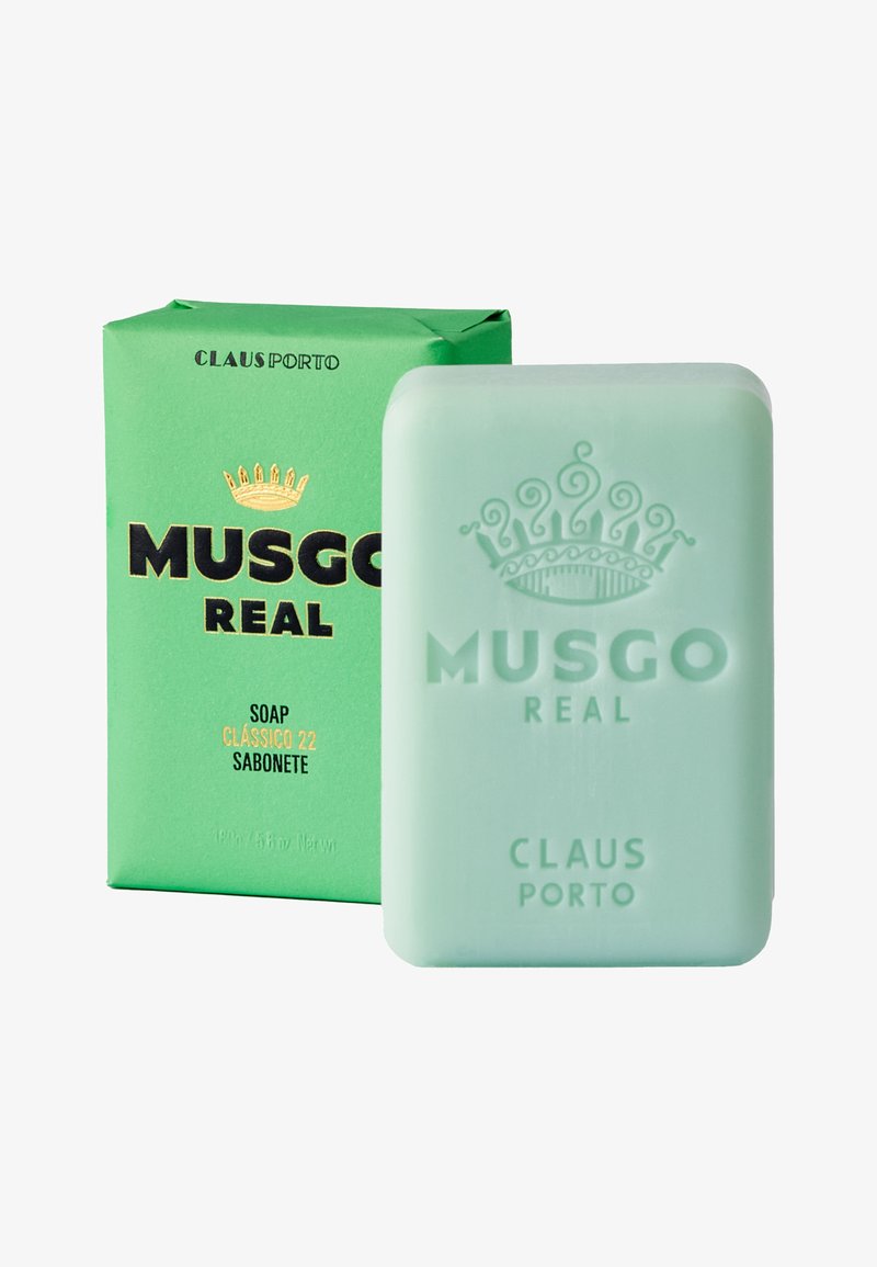Grüne Verpackung mit schwarzem und goldfarbenem Text zeigt ein halbtransparenter mintgrüner Seifenblock, der mit "MUSGO REAL" und einem Kronendesign geprägt ist.