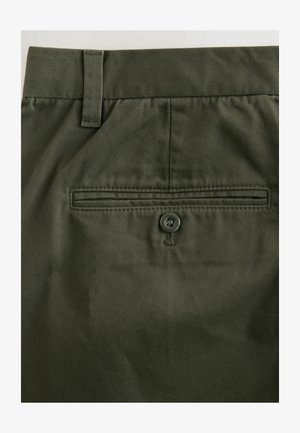 Tmavo zelené bavlnené nohavice so štandardným strihom, zadnou vreckom so zaistením na gombík a jemne textúrovanou tkaninou.
