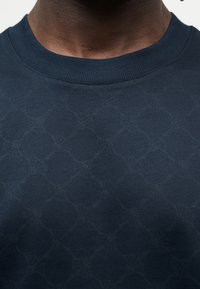 Μπλε ναυτικό φούτερ με υφασμάτινο σχέδιο, ριμπ λαιμόκοψη και κοντά μανίκια. Το ύφασμα φαίνεται μαλακό και ελαφρώς αντανακλαστικό.