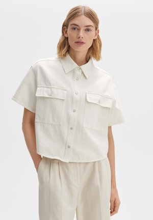 Cropped white denim shirt with short sleeves, featuring two chest pockets and snap buttons, textured fabric, and a pointed collar.