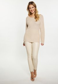 Beige neulepusero pitkillä hihoilla ja leveällä kaula-aukolla, yhdistettynä kermaisiin slim-fit-housuihin ja kultaisiin nauhakorkokenkiin. Tasainen pinta ja vartaloa myötäilevä malli.
