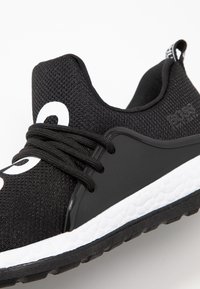 Zapatilla deportiva de malla negra con suela texturizada blanca, cordones negros y logo "BOSS" en el lateral y en la lengüeta del talón.