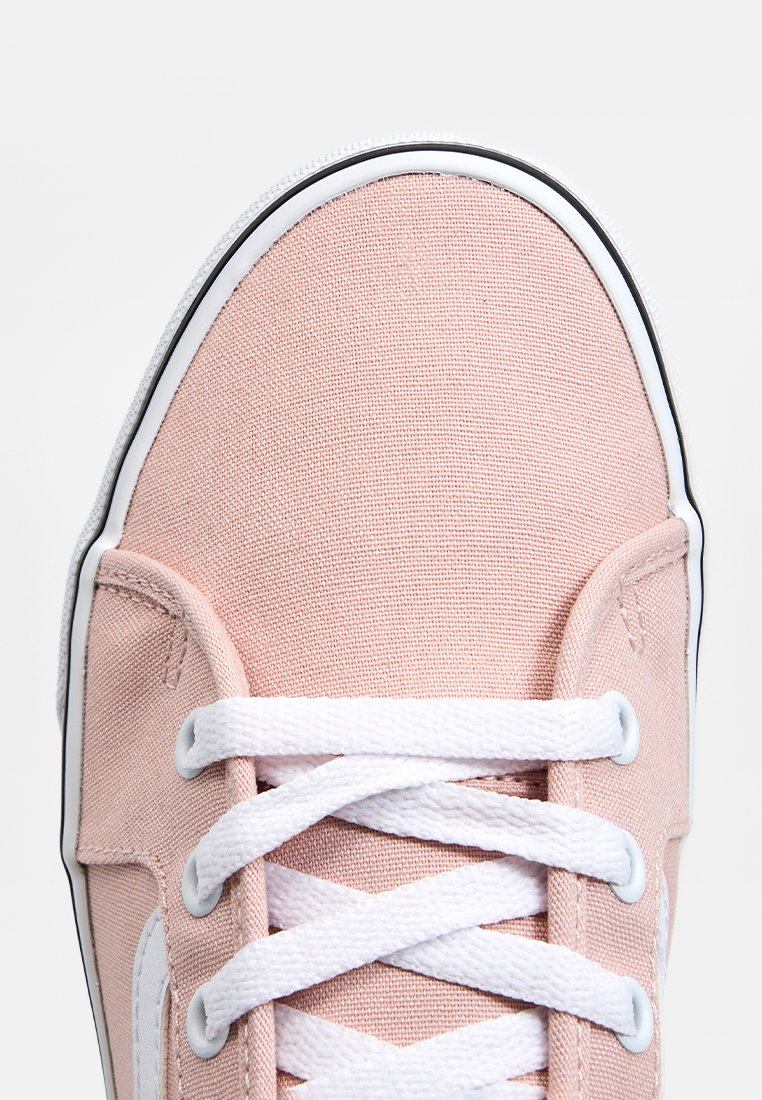 Zapatilla de lona rosa con cordones y costuras blancas. La puntera es redondeada y tiene una suela de goma blanca con borde negro.