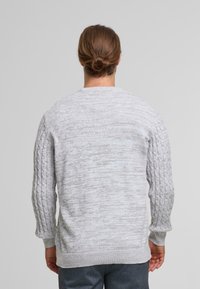 Suéter gris claro con mangas de punto trenzado texturizado y cuerpo liso. Puños y dobladillo acanalados. Diseño de cuello redondo, tejido de grosor medio.