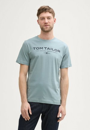 Lyseblå bomulds T-shirt med korte ærmer og rund halsudskæring. Har mørkeblå trykt tekst "TOM TAILOR" på forsiden.