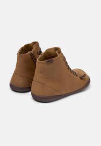 Botas de tobillo marrones con un acabado de piel suave, que presentan cordones y una cremallera lateral para facilitar su uso. La suela es oscura y ligeramente flexible.