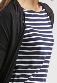 Sort let cardigan hængende over en marineblå stribet top med hvide striber; stoffet ser blødt ud med en afslappet pasform og rund halsudskæring.