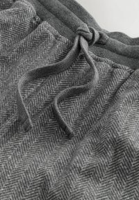 Graue Jogginghosen aus strukturiertem Stoff mit Fischgrätenmuster, ausgestattet mit einem elastischen Bund und einem Kordelzug zur Anpassung der Passform.