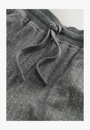 Šedé joggingové kalhoty vyrobené z texturované tkaniny s herringbonovým vzorem, mají elastický pas a šňůrku na nastavení velikosti.