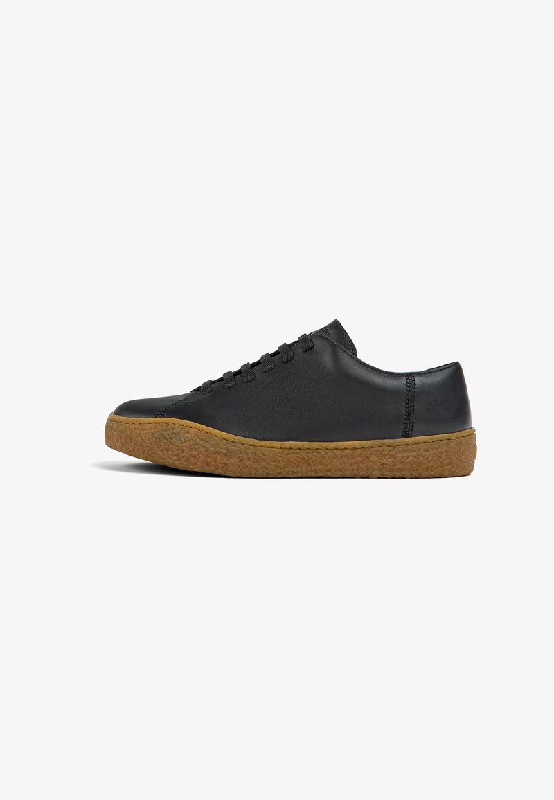 Black leather sneaker with a rounded toe, lace-up design, and textured tan rubber sole. Featuring subtle stitching accents.