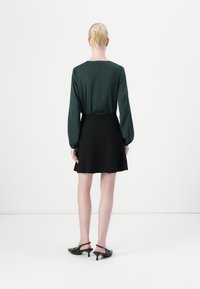 Groene satijnen top met lange mouwen, gecombineerd met een zwarte klokrok. De outfit heeft een soepele textuur en een eenvoudig ontwerp, aangevuld met zwarte hakken.