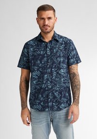 Camicia a maniche corte, blu navy, con bottini, decorata da un motivo tropicale di foglie azzurre; realizzata in un tessuto dalla consistenza liscia e un leggero lucido.