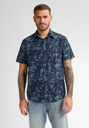 Camicia a maniche corte, blu navy, con bottini, decorata da un motivo tropicale di foglie azzurre; realizzata in un tessuto dalla consistenza liscia e un leggero lucido.