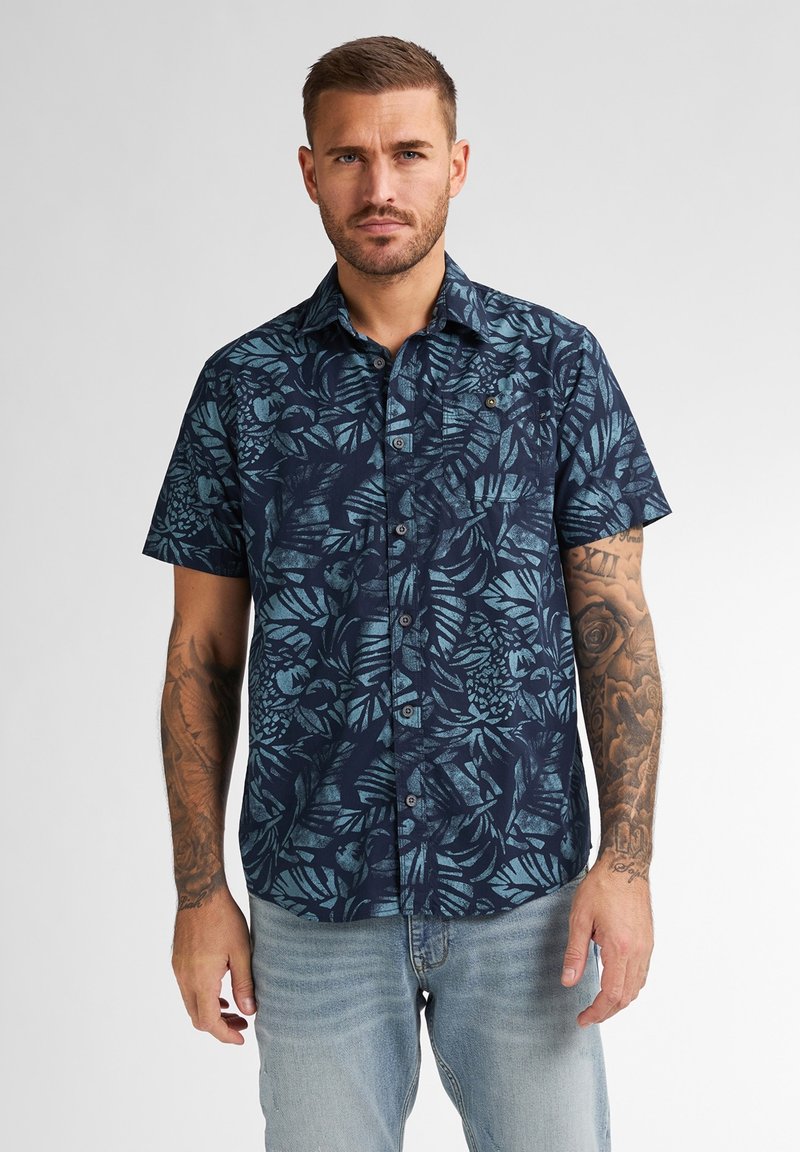 Camicia a maniche corte, blu navy, con bottini, decorata da un motivo tropicale di foglie azzurre; realizzata in un tessuto dalla consistenza liscia e un leggero lucido.