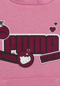 Felpa rosa con un grande logo “PUMA” nero e bordeaux, insieme a grafiche di Hello Kitty e piccoli cuori decorativi. Materiale in cotone, design casual.