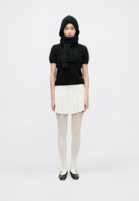 Čierny mäkký pletený top s krátkymi rukávmi v kombinácii s bielou skladanou sukňou. Modelka má na nohách čierne balerínky a svetlé pančuchy.