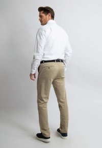 Lichtgewicht witte overhemd met lange mouwen gecombineerd met beige broek; heeft een slim fit, knoopmanchetten en een donkere riem; gedragen met donkere schoenen.
