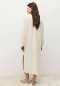 Robe longue couleur crème avec des manches bouffantes, fentes latérales et coupe décontractée, fabriquée en tissu léger, vue de dos.
