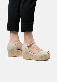 Beiga kilklack-sandaler med en flätad jutesula, nätinslag, ankelrem och öppen tå-design. Har ett litet dekorativt emblem.