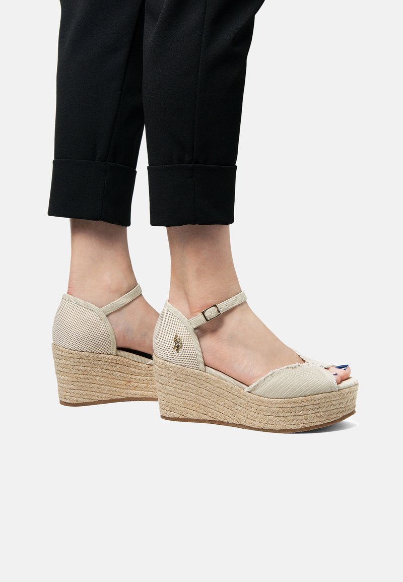 Beiga kilklack-sandaler med en flätad jutesula, nätinslag, ankelrem och öppen tå-design. Har ett litet dekorativt emblem.