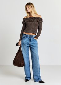 Haut marron à épaules dénudées avec volants texturés, associé à un jean large bleu clair et un sac à épaule en cuir suédé marron foncé.