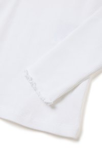 Camiseta blanca de manga larga con textura acanalada, que presenta puños deshilachados y un dobladillo redondeado. La tela tiene una textura suave con un patrón de acanalado visible.