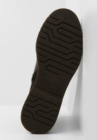 Zwarte schoenen zool met een gestructureerd, profiel patroon. Gemaakt van rubber, met een ronde vorm en een versterkte rand. Merklogo zichtbaar.