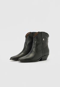 Botines de cuero negro hasta el tobillo con punta afilada, que presentan detalles de costura y tiradores, complementados por un pequeño tacón y acentos en hardware plateado.