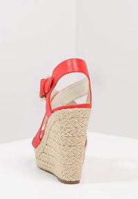 Sandalo rosso con tacco in juta intrecciata, cinturino alla caviglia regolabile e tomaia in pelle liscia. Presenta un'accento a fiocco sul cinturino alla caviglia.