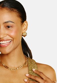 Zlaté šperky zahŕňajú kruhové náušnice a náhrdelník s článkovým reťazcom s perlovými akcentmi, nosené so zlatým trblietavým topom.