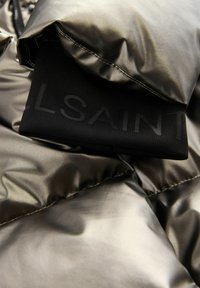Metallic olivgrüne Pufferjacke mit glänzender Oberfläche, die an den schwarzen Stoffbündchen mit "ALLSAINTS" beschriftet ist. Glatte Textur und gestepptes Muster.