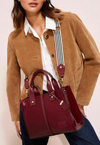 Bordo odinė rankinė su dviem rankenomis ir dryžuota petneša. Papuošta auksinės spalvos detalėmis ir turi elegantišką, stuktūrizuotą dizainą.