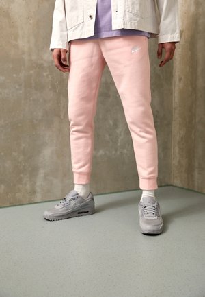 Light pink sweatpants with cuffed ankles, paired with gray Nike sneakers and white crew socks, worn with a light jacket over a purple shirt.