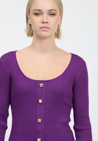 Lila ribbed Langarmshirt mit weitem Rundhalsausschnitt, versehen mit fünf quadratischen goldenen Knöpfen auf der Vorderseite. Glatter Strickstoff.