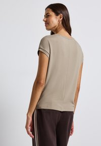 Beige kortemouwen top gemaakt van zacht materiaal, met een ronde halslijn, een relaxte pasvorm en een subtiele naaddetails langs de achterkant.