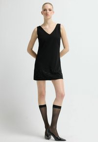 Czarna sukienka bez rękawów z dekoltem w szpic i misternym zdobieniem z koralików przy dole. Noszona z czarnymi, przezroczystymi zakolanówkami i czarnymi szpilkami z ostrym noskiem.