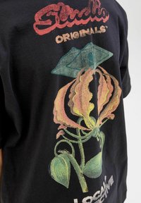 Černé bavlněné tričko se živou barevnou grafickou koncepcí květin, v odstínech růžové, žluté a zelené, spolu s textem "Studio Originals".