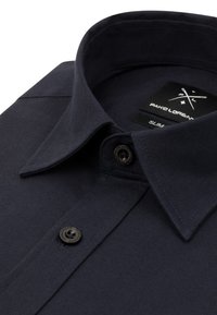 Ciemnoniebieska koszula slim fit z kołnierzykiem zapinanym na guziki, z pojedynczym czarnym guzikiem i tkanym wzorem. Metka głosi "PAKO LORENT."