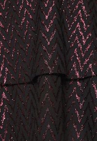 Svart tyg med ett zigzag-mönster i glittrande burgundyröda paljetter, med en lagerdesign och texturerade detaljer genom hela.