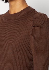 Brauner gerippter Pullover mit Rundhalsausschnitt und subtilen Puffärmeln, aus einem weichen, strukturierten Strickstoff gefertigt.