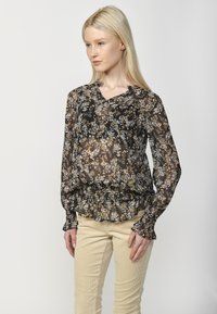 Blusa nera a fiori con maniche lunghe, scollatura a V e vita arricciata. Presenta piccoli fiori bianchi e marroni su un tessuto trasparente. Texture leggera e fluida.