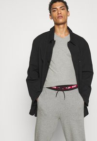 Cămașă neagră cu nasturi peste un tricou gri cu guler în V și pantaloni de trening gri, având un brâu colorat și un fit lejer.