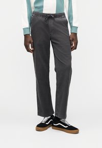 Γκρι παντελόνι σε χαλαρή εφαρμογή με ελαστική μέση και κορδόνι. Διαθέτει πλαϊνές τσέπες και διακριτικές ραφές σε αντίθεση. Φορεμένο με μαύρα αθλητικά παπούτσια.