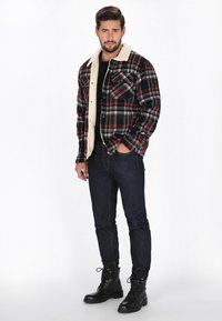 Kockás flanel dzseki fekete, piros és szürke színben, krém színű gyapjú gallérral, két szívzsebbel és gombos záródással. Fekete ing fölött viselt.