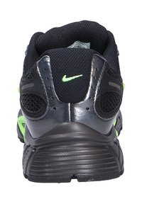 Zapatilla deportiva negra con parte superior de malla, acentos en verde neón y suela de goma texturizada. Incluye un discreto logotipo de Nike en la parte trasera.