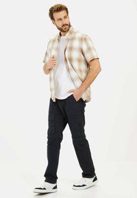 Kurzarm kariertes Hemd in Creme, Orange und Grün über einem weißen T-Shirt, kombiniert mit dunklen Cargo-Hosen und weißen Sneakers. Lässiger Schnitt.