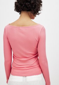 Ribbad rosa långärmad topp med bred båtringning, åtsittande form och slät yta. Bakifrån visas söms detaljer och åtsittande passform.
